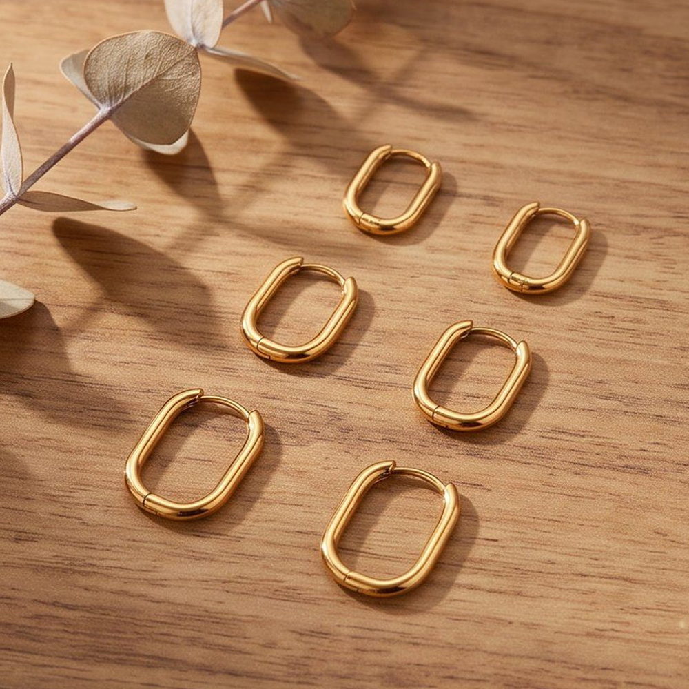 Six gold-tone huggie earrings in different sizes laid out in rows on a warm wood surface