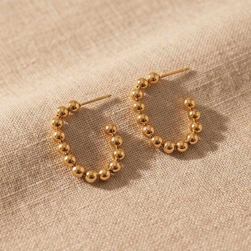 Gold-tone beaded huggie earrings with a row of small beads along the outer face