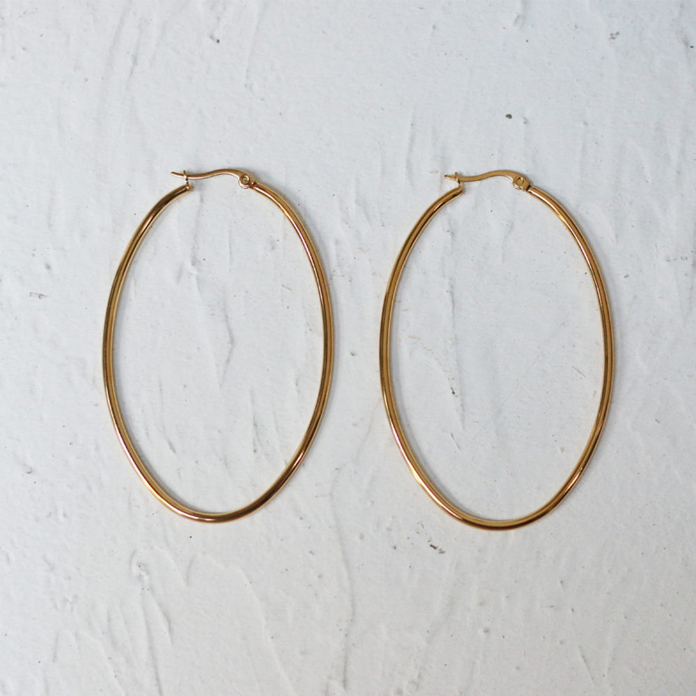 Two large thin gold-tone hoop earrings standing against a pale stone surface
