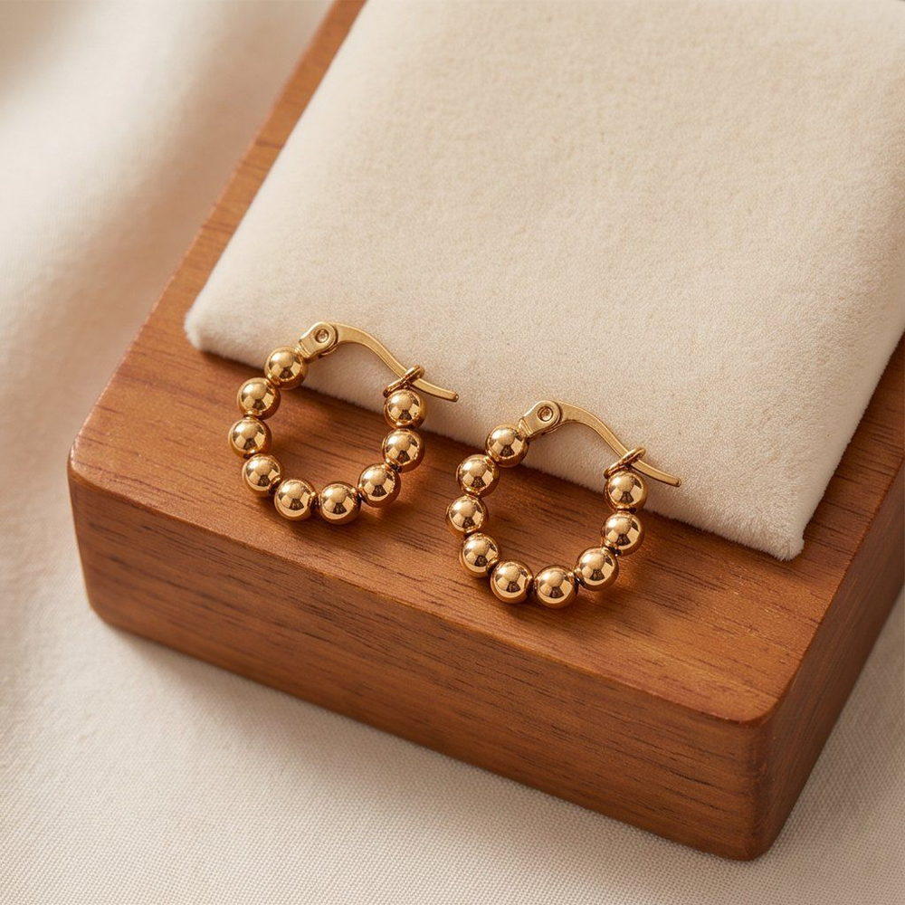 Two gold-tone bead-textured huggie earrings presented on a wooden block