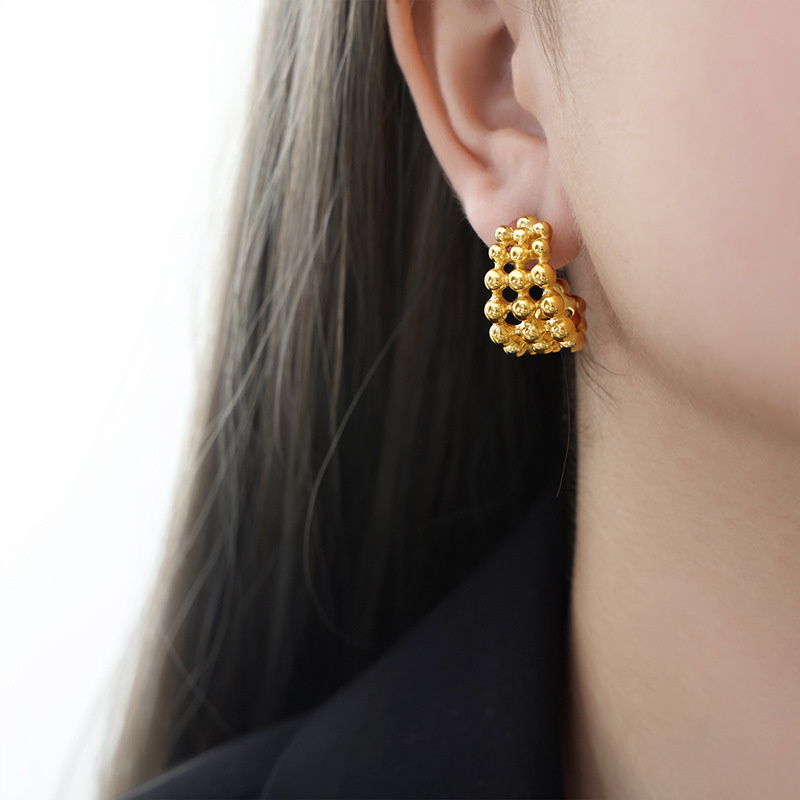 Close view of a beaded gold-tone hoop earring worn on the ear