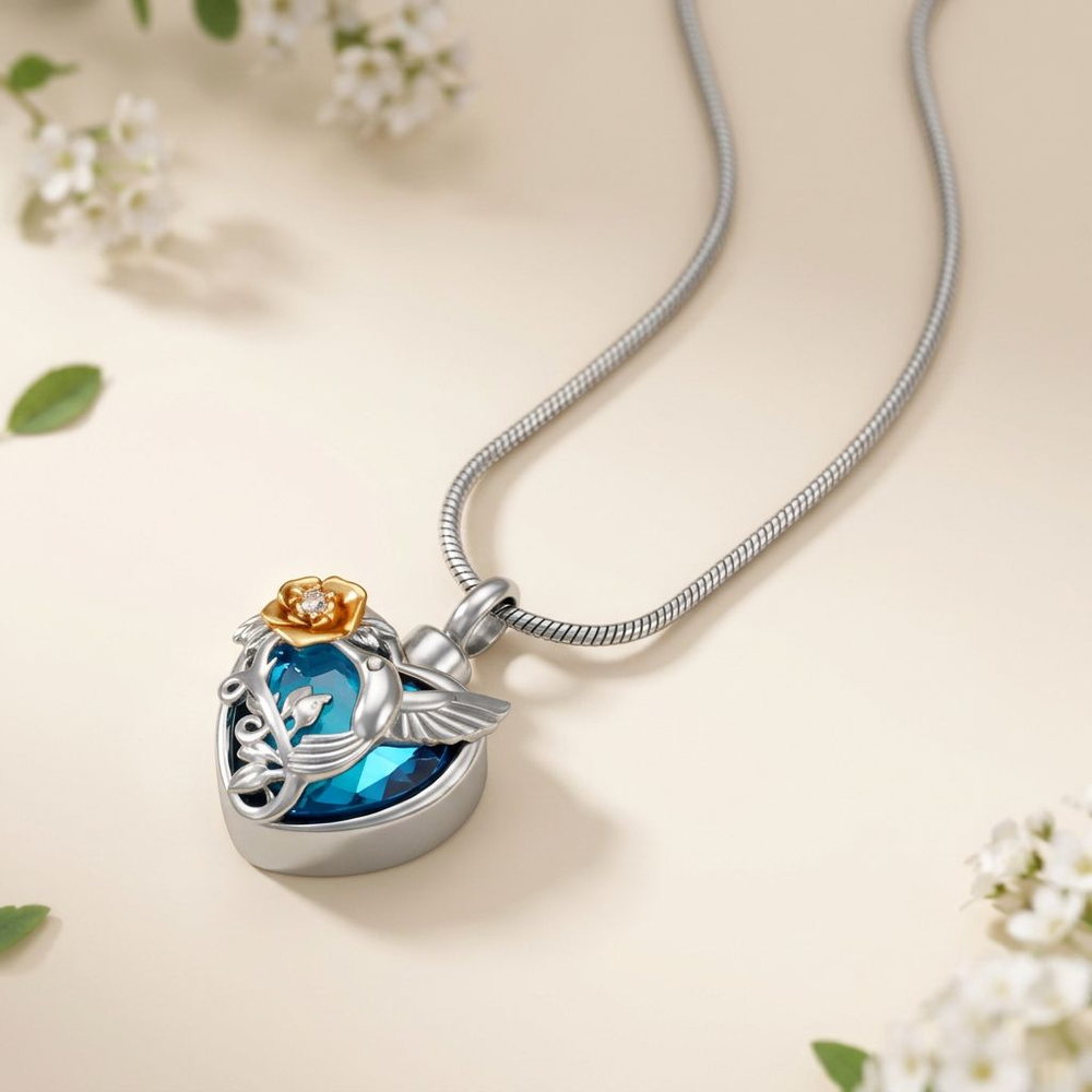 A steel heart pendant set with a blue crystal heart, finished with a hummingbird relief and a small gold rose